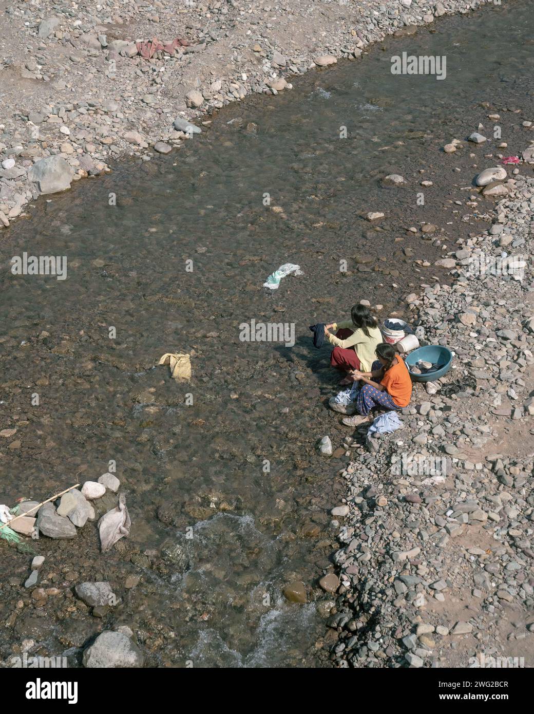 Two Nepali children wash clothes in the river A mountain view looking out over a lush green valley in Birendranagar, Karnali Province, Western Nepal. Stock Photo