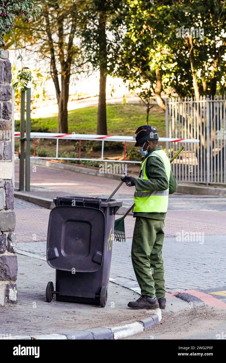 black African man sweeping streets and cleaning up, street cleaner dressed in overall and hi visibility work clothes in South Africa Stock Photo