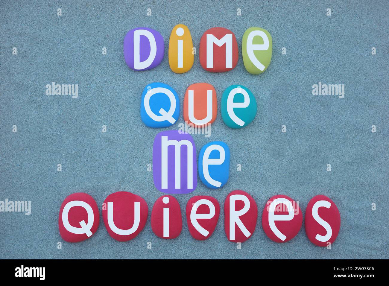 Dime que me quieres, tell me you love me, spanish text composed with hand painted multi colored stone letters over green sand Stock Photo