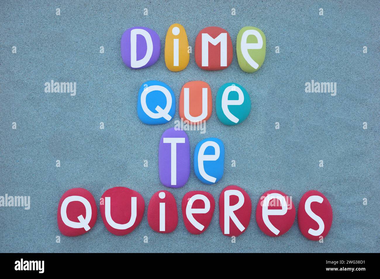 Dime que te quieres, tell me he loves you, spanish love text composed with hand painted multi colored stone letters over green sand Stock Photo