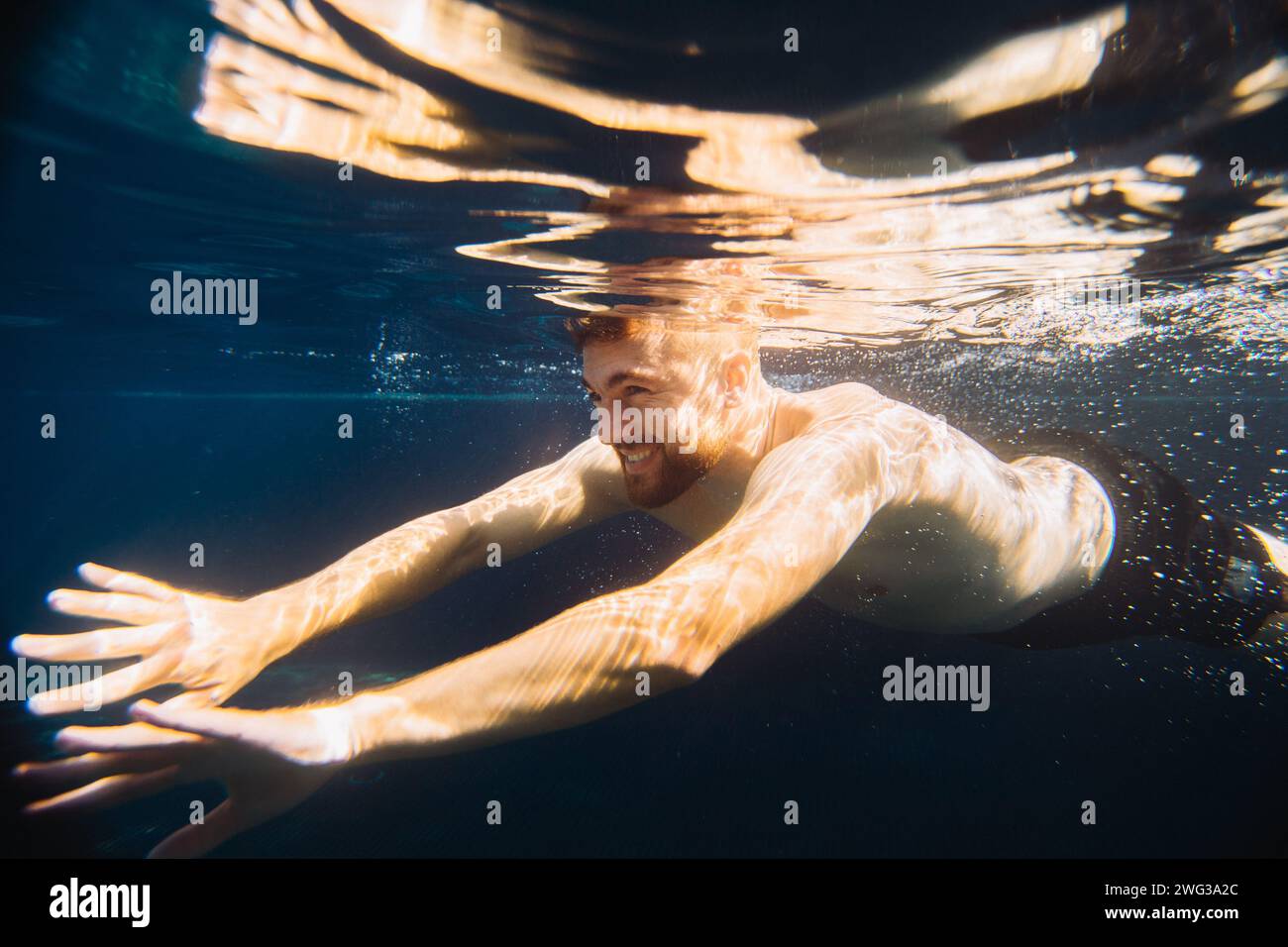 A handsome young man swims underwater in a swimming pool while on ...