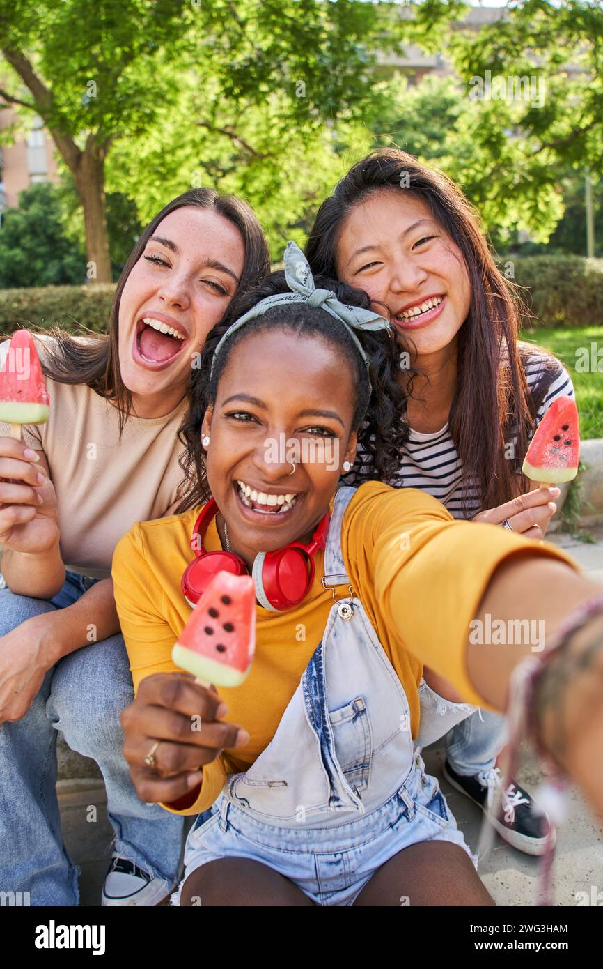 Close up faces three smiling young multi-ethnic women outdoors eating ice cream. Concept friendship. Stock Photo