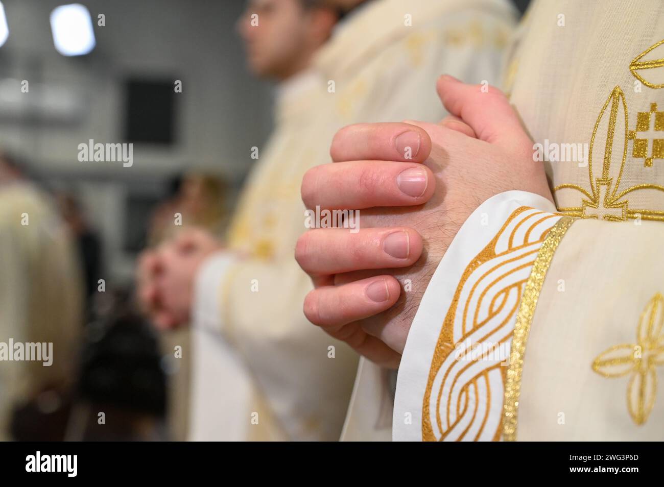 Catholic priests in liturgical vestments praying with hands folded. Hands of Christian man praying in Cathedral. Christmas Midnight Mass in church. Stock Photo