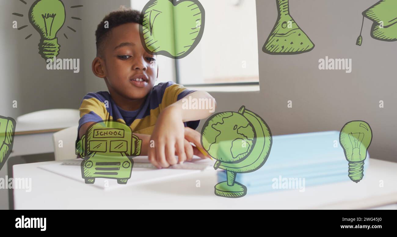 Image of green school icons over happy african american schoolboy working at desk in class Stock Photo