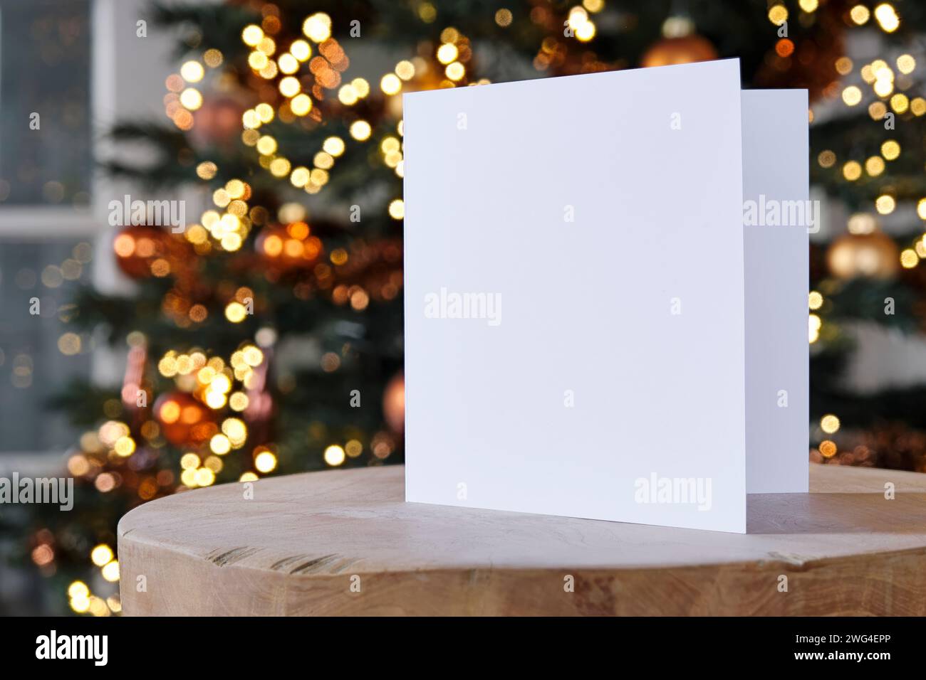 Standing blank empty square greeting card mock up before a blurred christmas tree with copy space. For use as a Christmas, background template. Stock Photo
