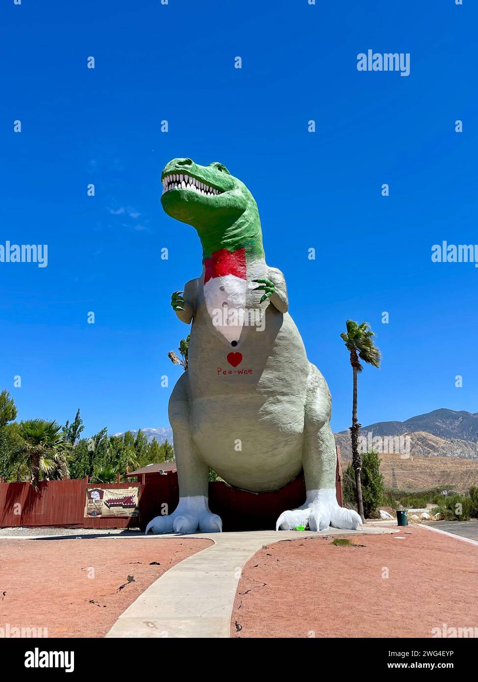 Statue of dinosaur wearing inflatable hat perched on a bench Stock Photo