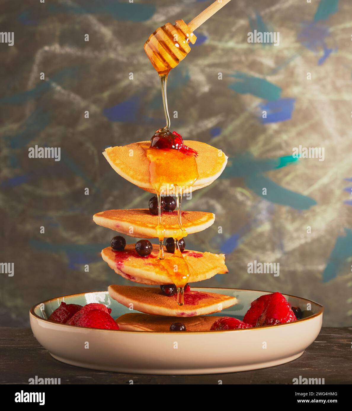 Flying pancakes with mixed berries and honey being drizzled over them. Stock Photo