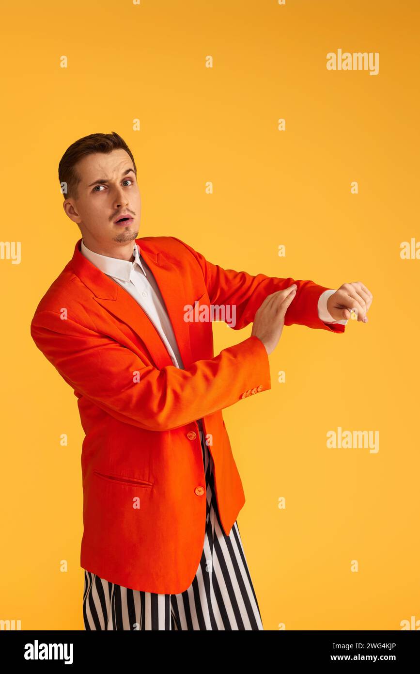 Cheerful funny young man in orange jacket and striped pants on yellow ...