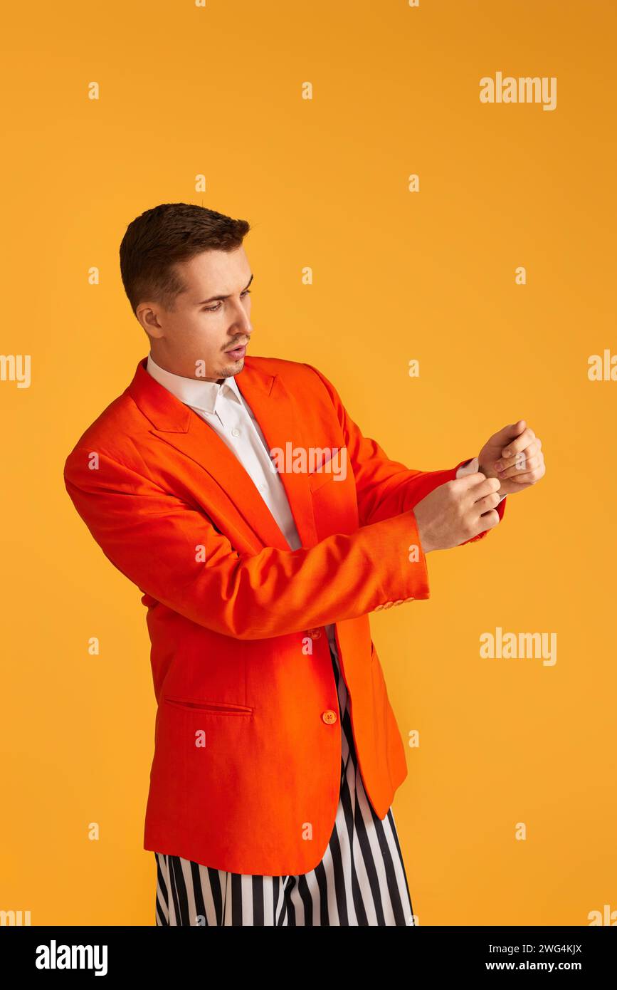 Cheerful funny young man in orange jacket and striped pants on yellow ...