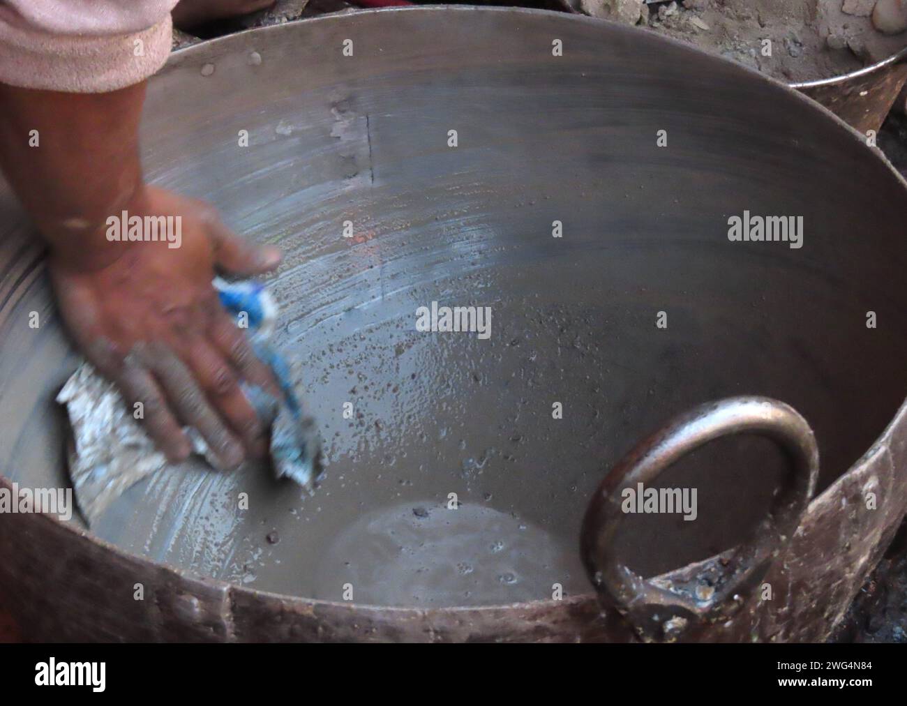An action motion shot of a man cleaning a large cooking pot with sand and grit with a dirty cloth and water. Cooking eating out hygiene concept Stock Photo