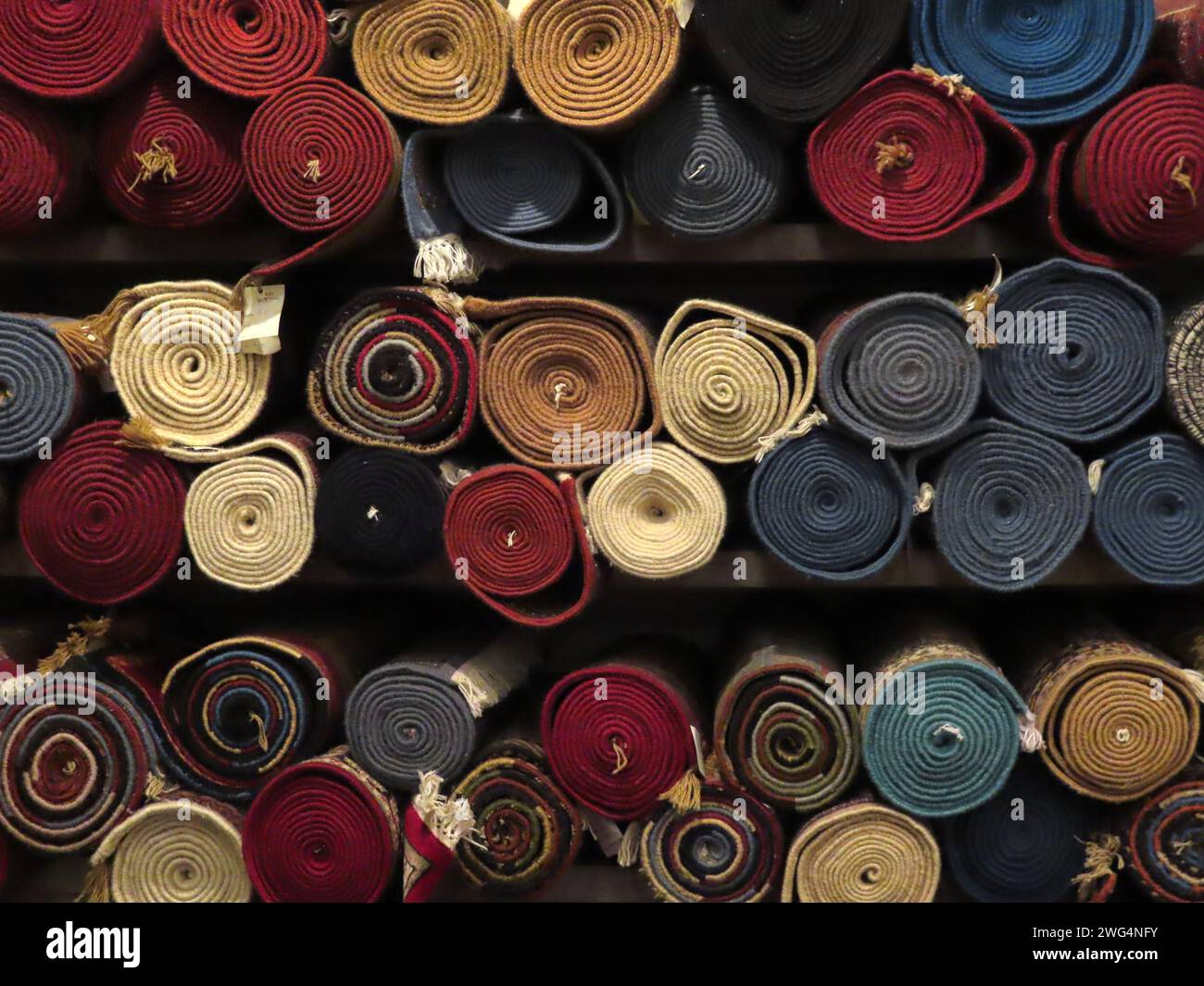 A front on view of a variety of tightly rolled colorful handmade authentic traditional patterned woolen or cashmere floor rugs. Rugs or floor mats on Stock Photo