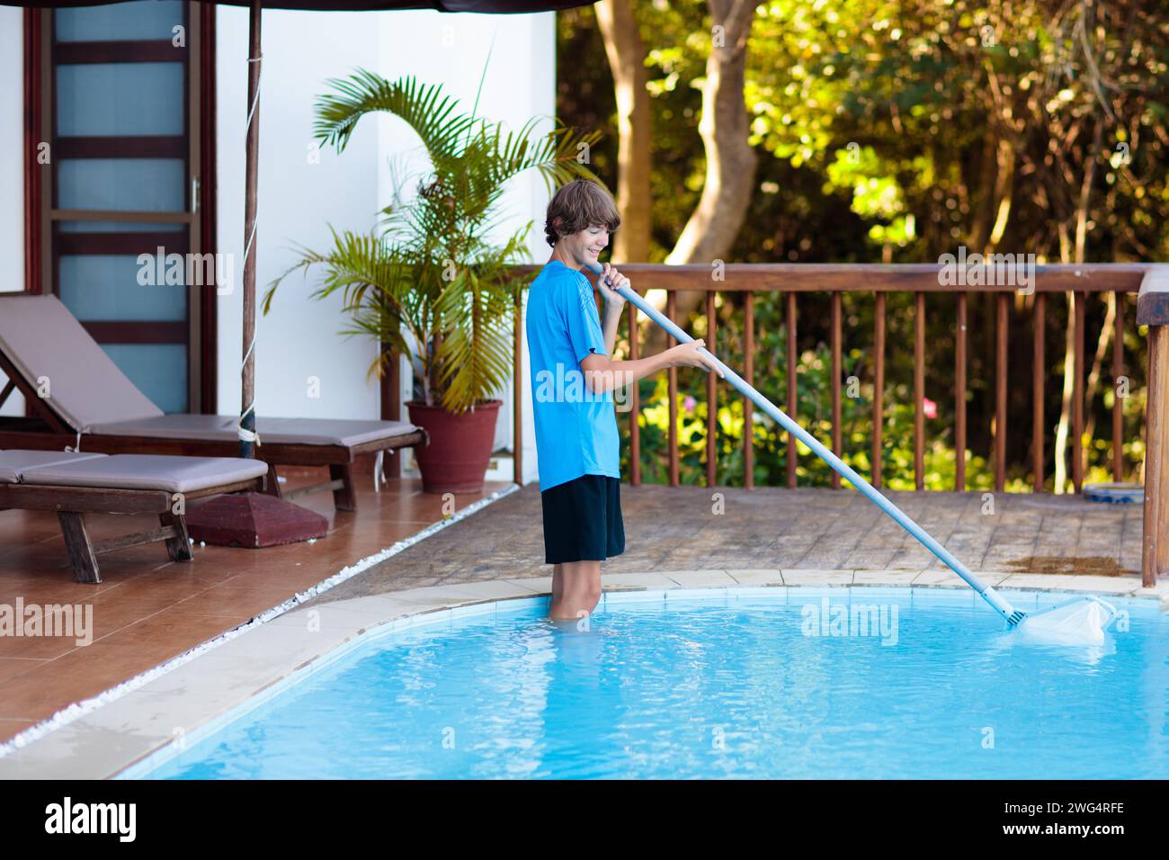 Boy cleaning swimming pool. Maintenance and service for outdoor pool. Teenager after school job and house help. Teen student picking foliage leaf Stock Photo
