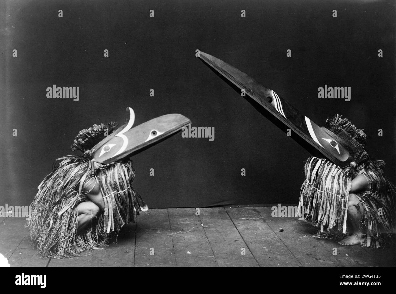 Kotsuis and Hohhug-Nakoaktok, wearing ceremonial dress, with long beaks, on their haunches, dancing(?), c1914. Stock Photo