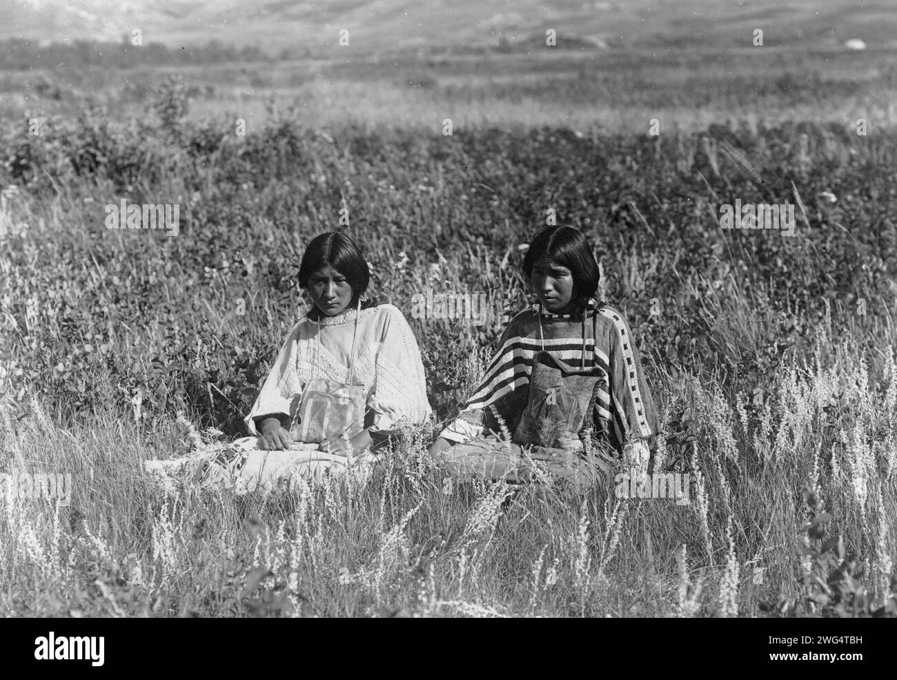 Little Plume's daughter, c1910. Two young Piegan women seated in tall grass. Stock Photo