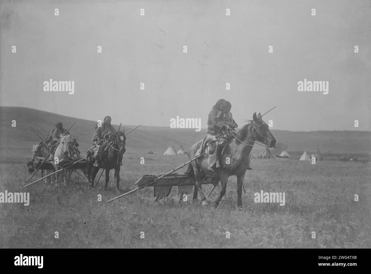 Moving camp-Atsina, c1908. Several Atsina on horses with travois behind them, tipis in background. Stock Photo