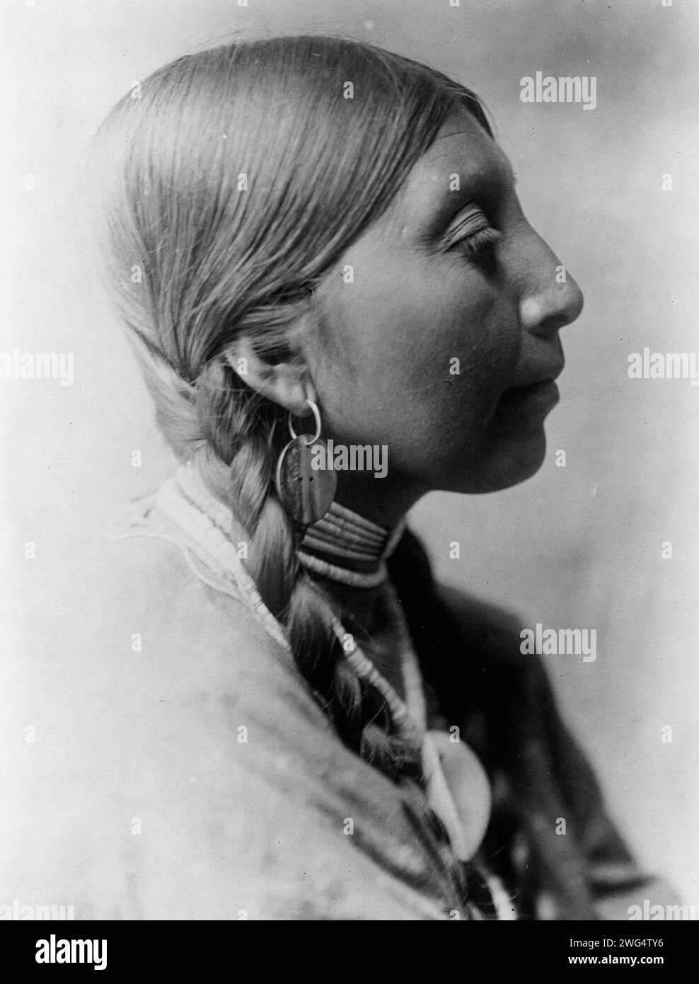 Wishham young woman, c1910. Chinookan Indians: Tlakluit; Washington. Head-and-shoulders portrait of young Wishham Indian woman, facing right, wearing braids, shell bead choker, and abalone shell disk earrings. Stock Photo