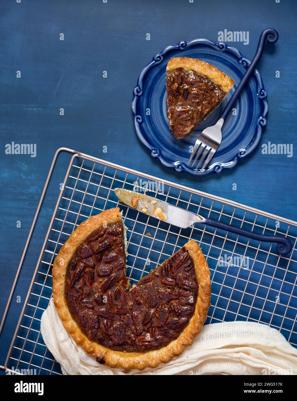 Overhead view of a pecan pie on a cooling rack on a blue surface with a ...