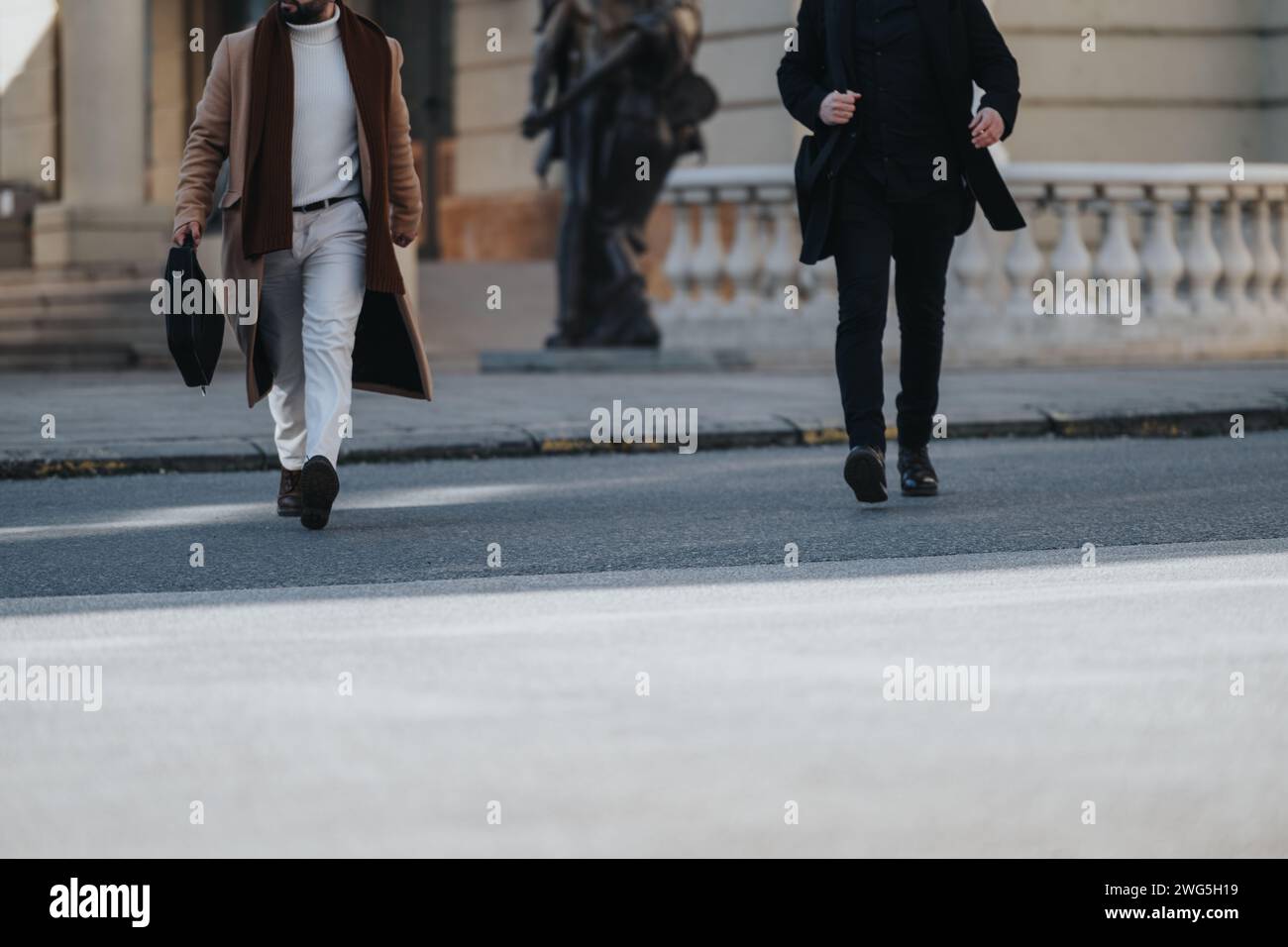 Captured mid stride, this image depicts two men in business attire confidently crossing an urban street, showcasing style and purpose. Stock Photo
