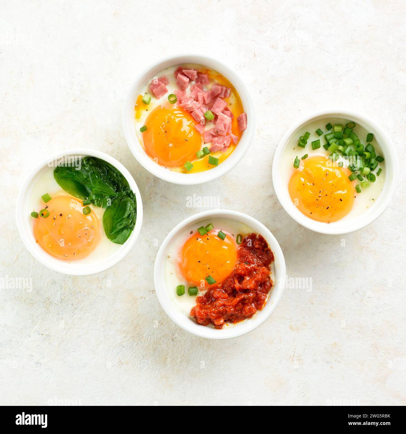 Eggs en cocotte (baked eggs) in ramekins over light background. Healthy