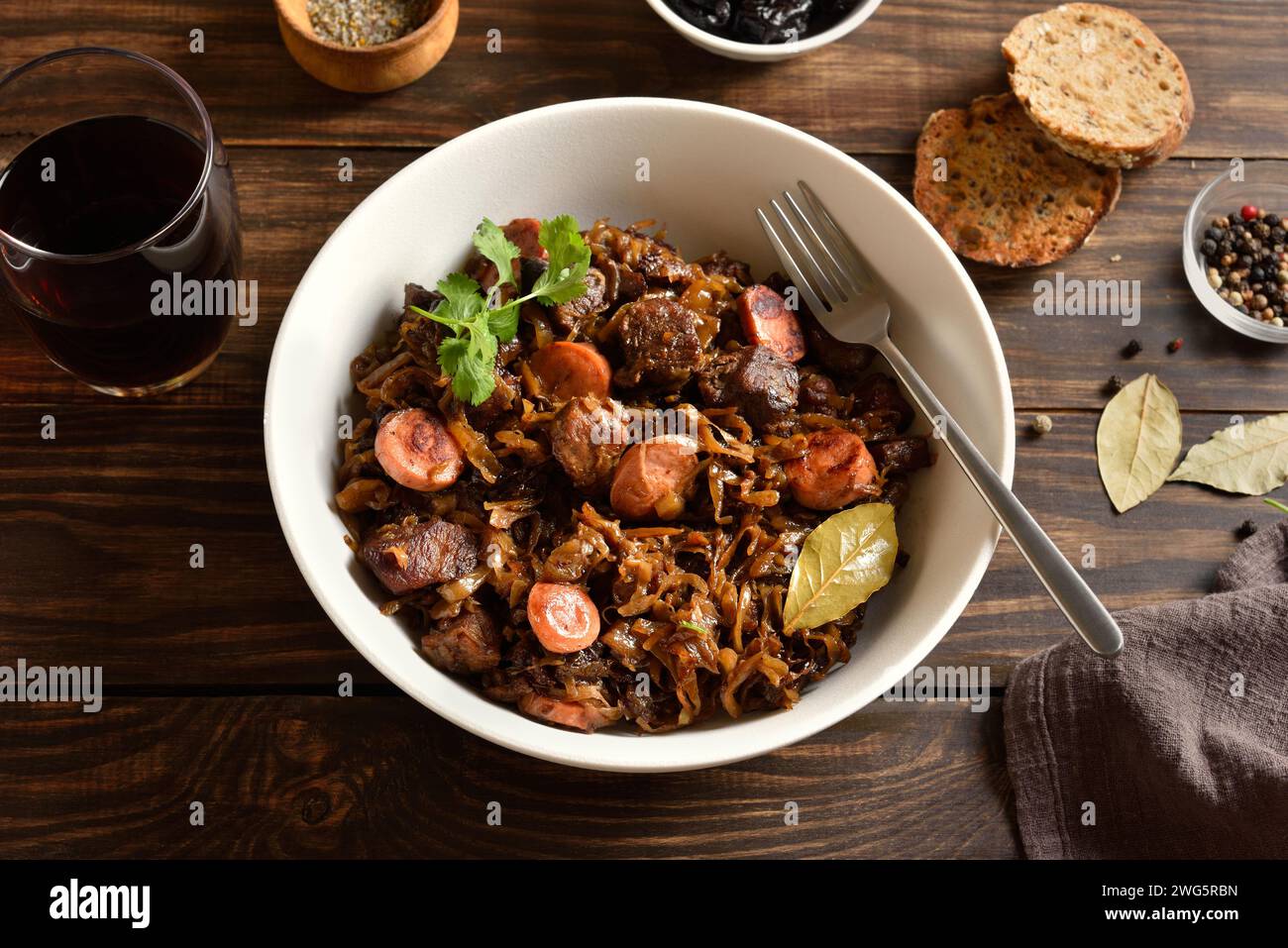 Stewed cabbage (polish bigos) with sauerkraut, mushrooms, smoked meats and spices in bowl over wooden background. Close up view Stock Photo