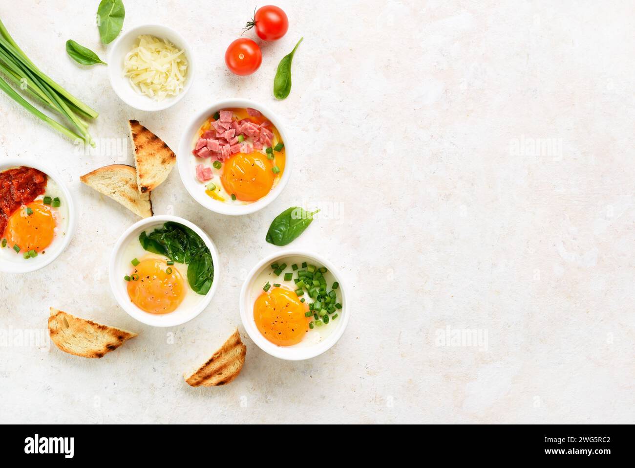 Eggs en cocotte (baked eggs) in portion ceramic bowl over light background with free space. Healthy morning food concept. Top view, flat lay Stock Photo