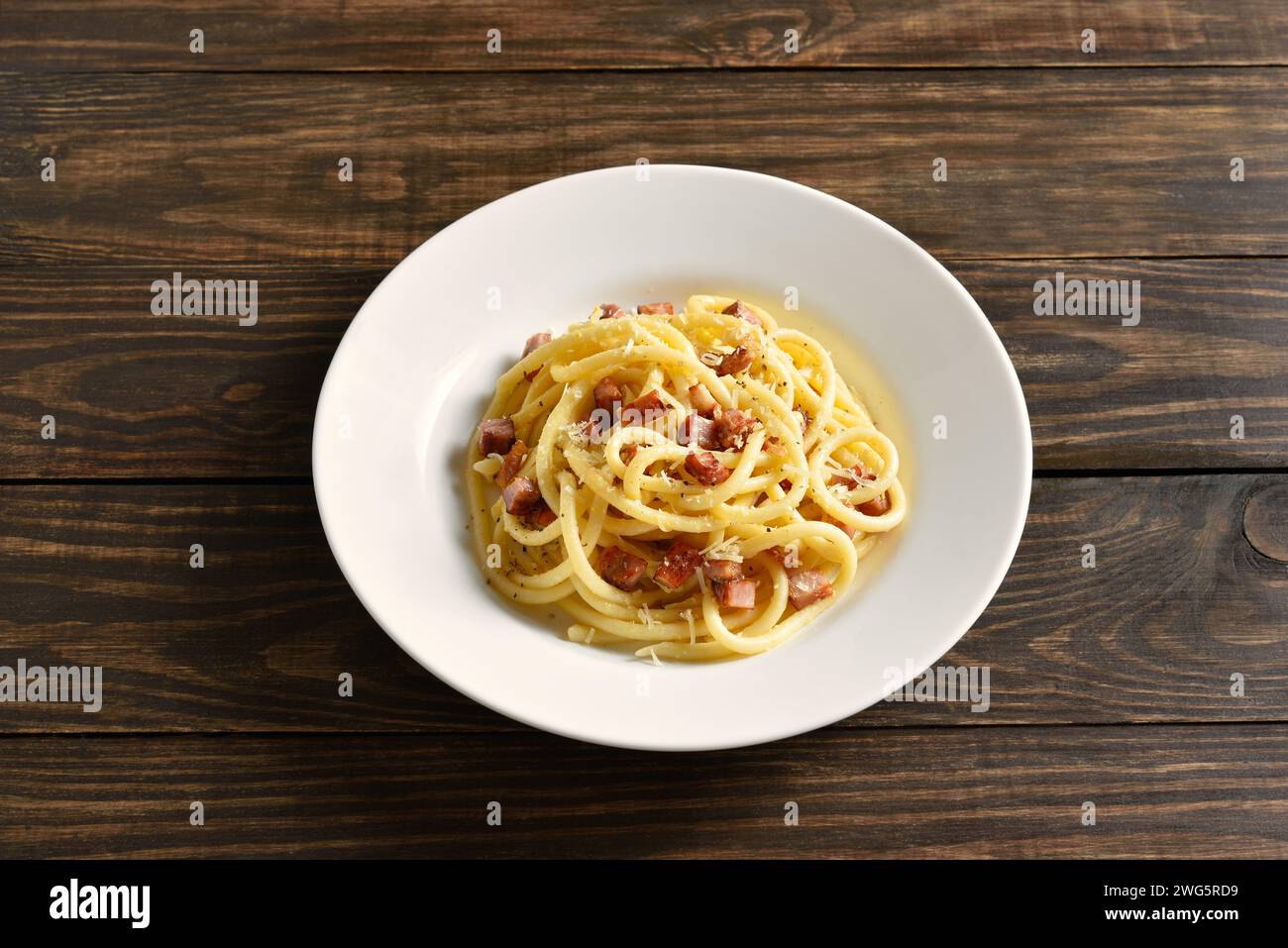 Carbonara pasta, spaghetti with crisp pancetta bacon and black pepper on white plate over rustic wooden background. Close up view Stock Photo