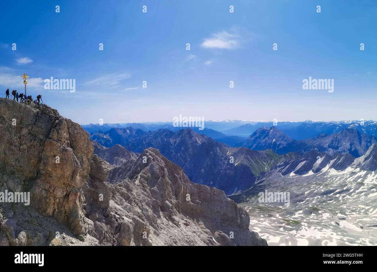 the summit cross of zugspitze with a group of people and view to the alps at sunny clear blue sky Stock Photo