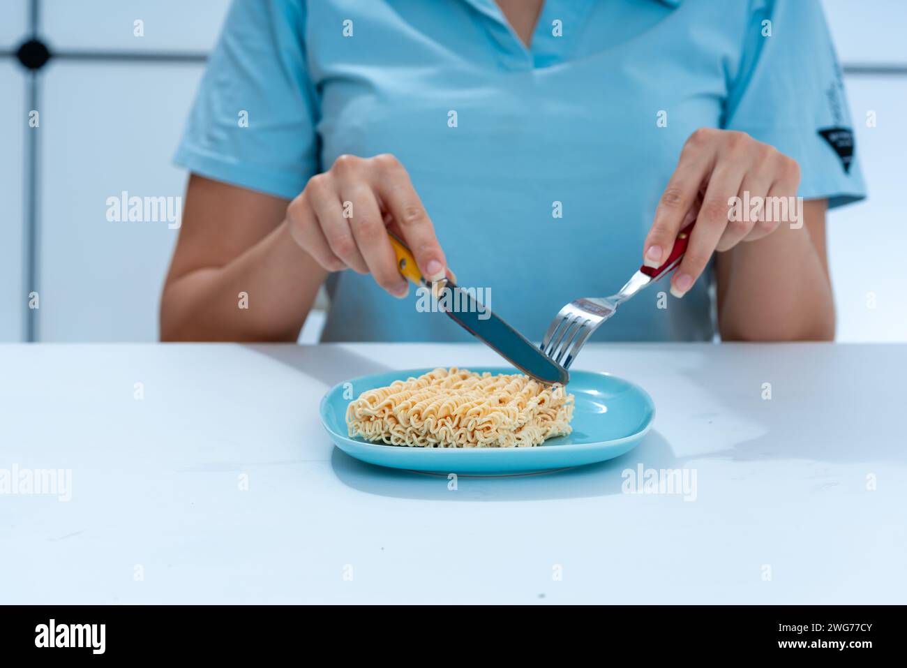 girl sitting at the table on the table a plate with a block of instant noodles the concept of unhealthy food Stock Photo