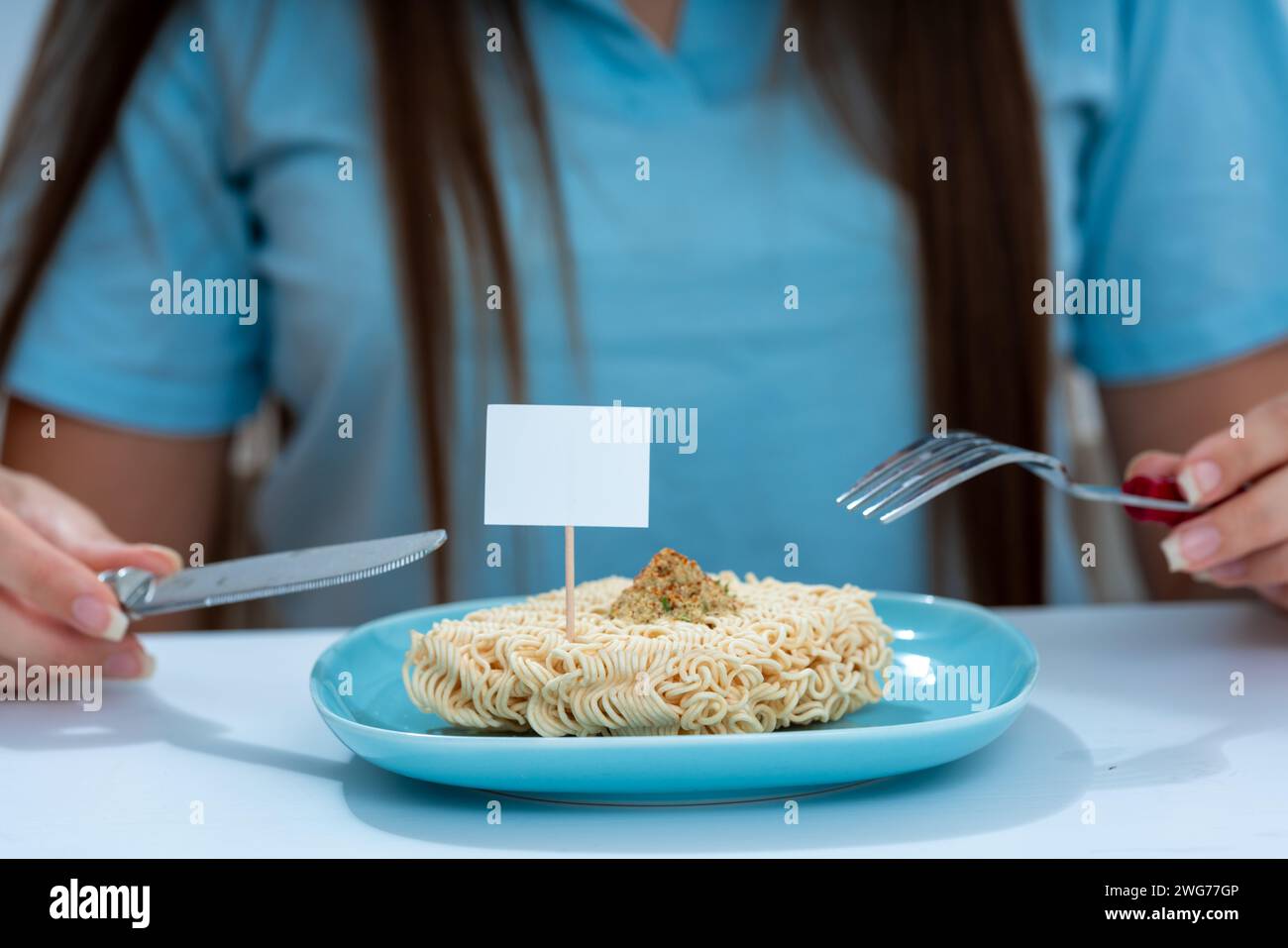 girl sitting at the table on the table a plate with a block of instant noodles the concept of unhealthy food Stock Photo
