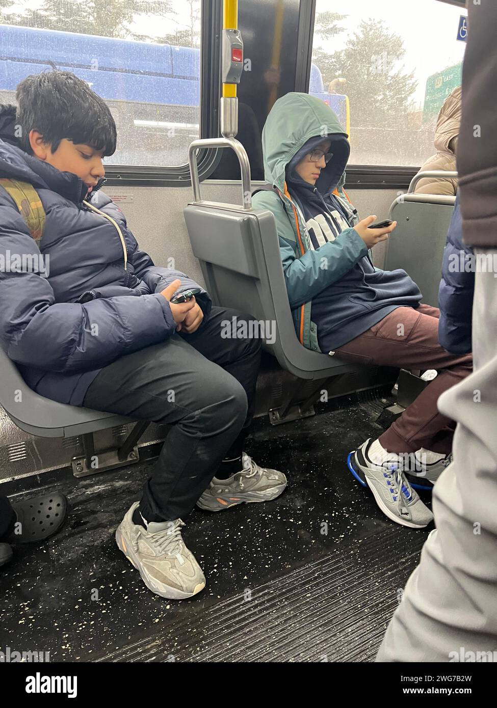 School boys riding a city bus to school glued to their phones in Brooklyn, New York. Stock Photo