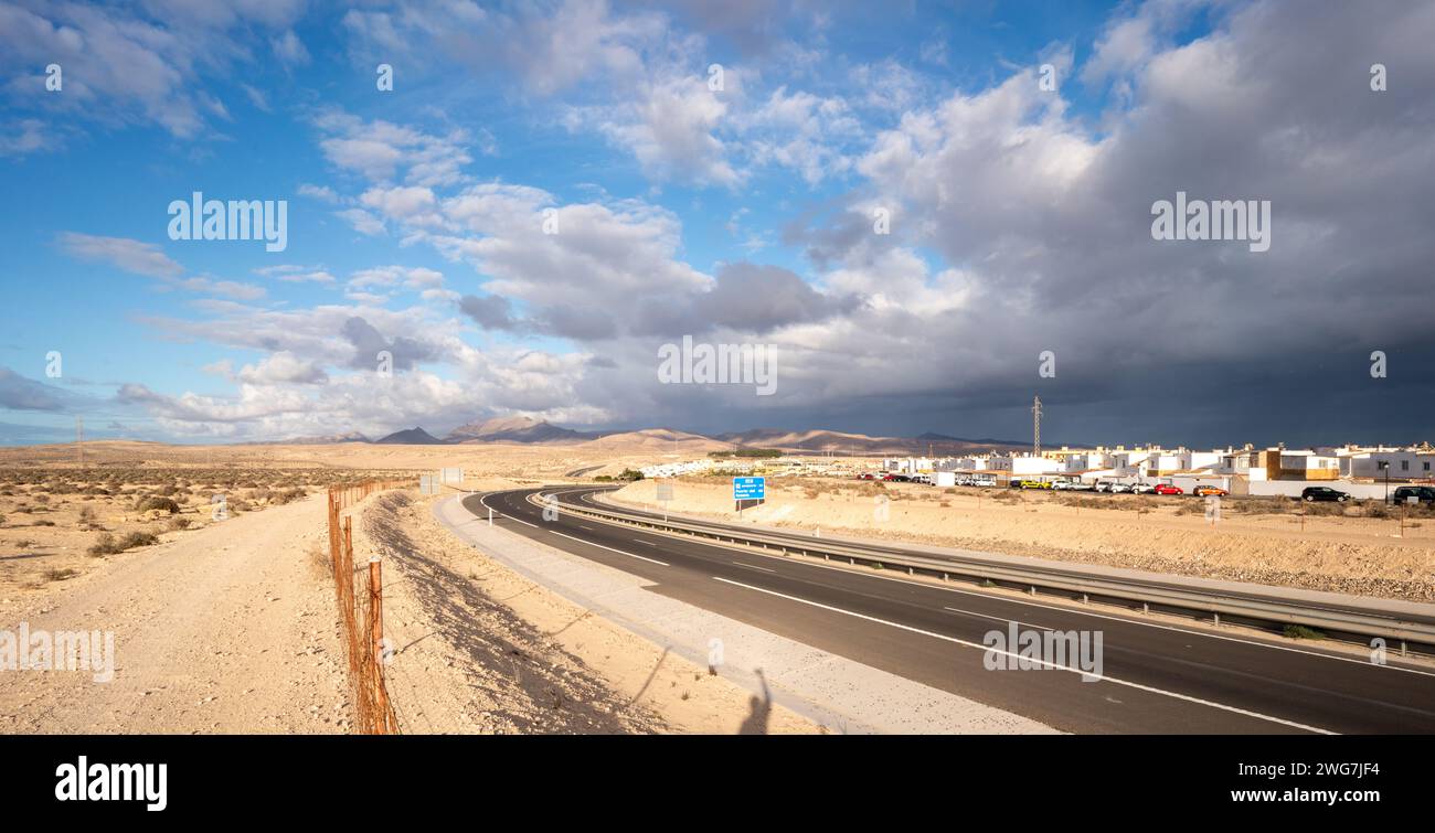 A desert highway with a shadow on the side of the road. The shadow is from a lone tree, and it is the only thing that breaks up the monotony of the de Stock Photo