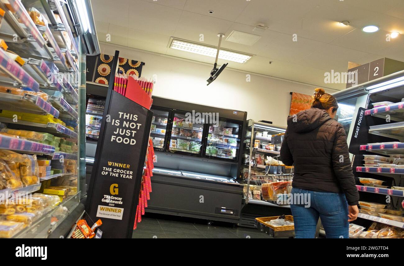 M&S store interior rear back woman looking at food on shelf The Grocer Gold Awards sign grocer of the year award in aisle inside store 2023 UK Stock Photo