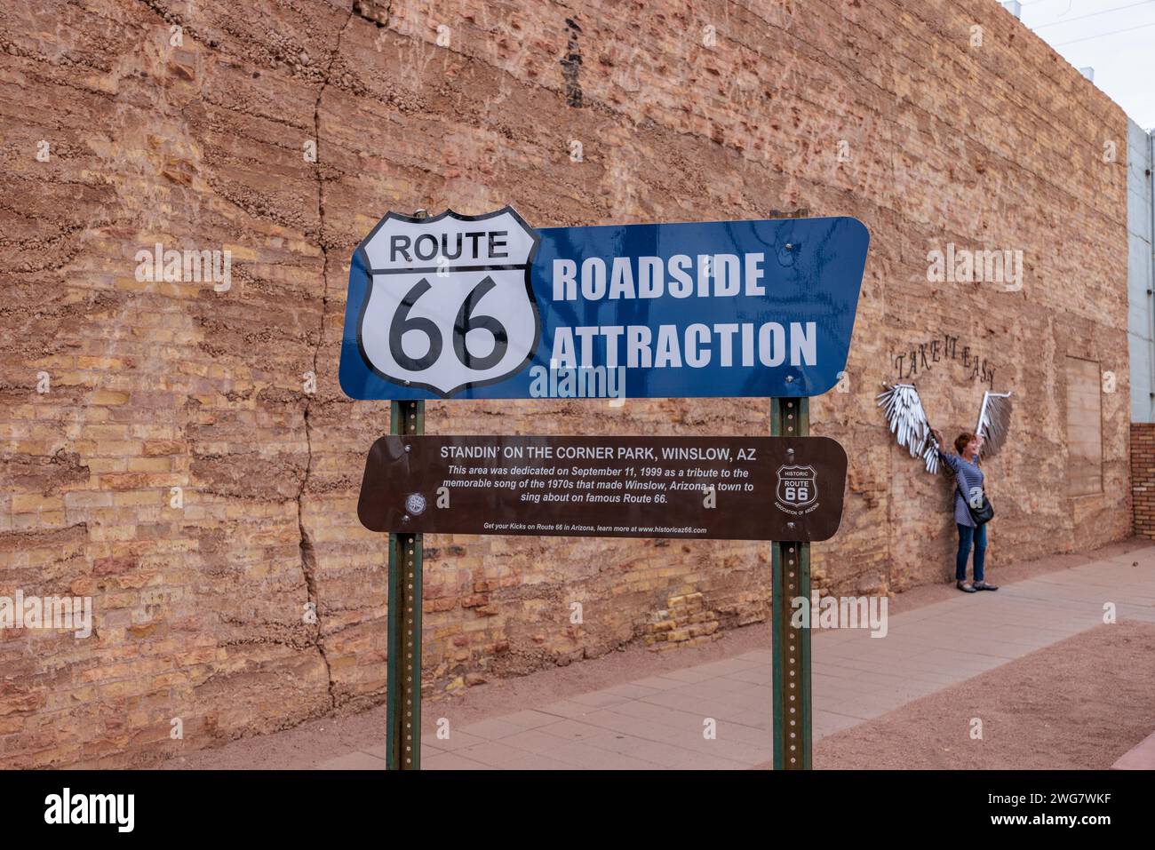Woman posing for a photo behind roadside attraction sign at Standin' on the Corner Park in downtown Winslow, Arizona Stock Photo