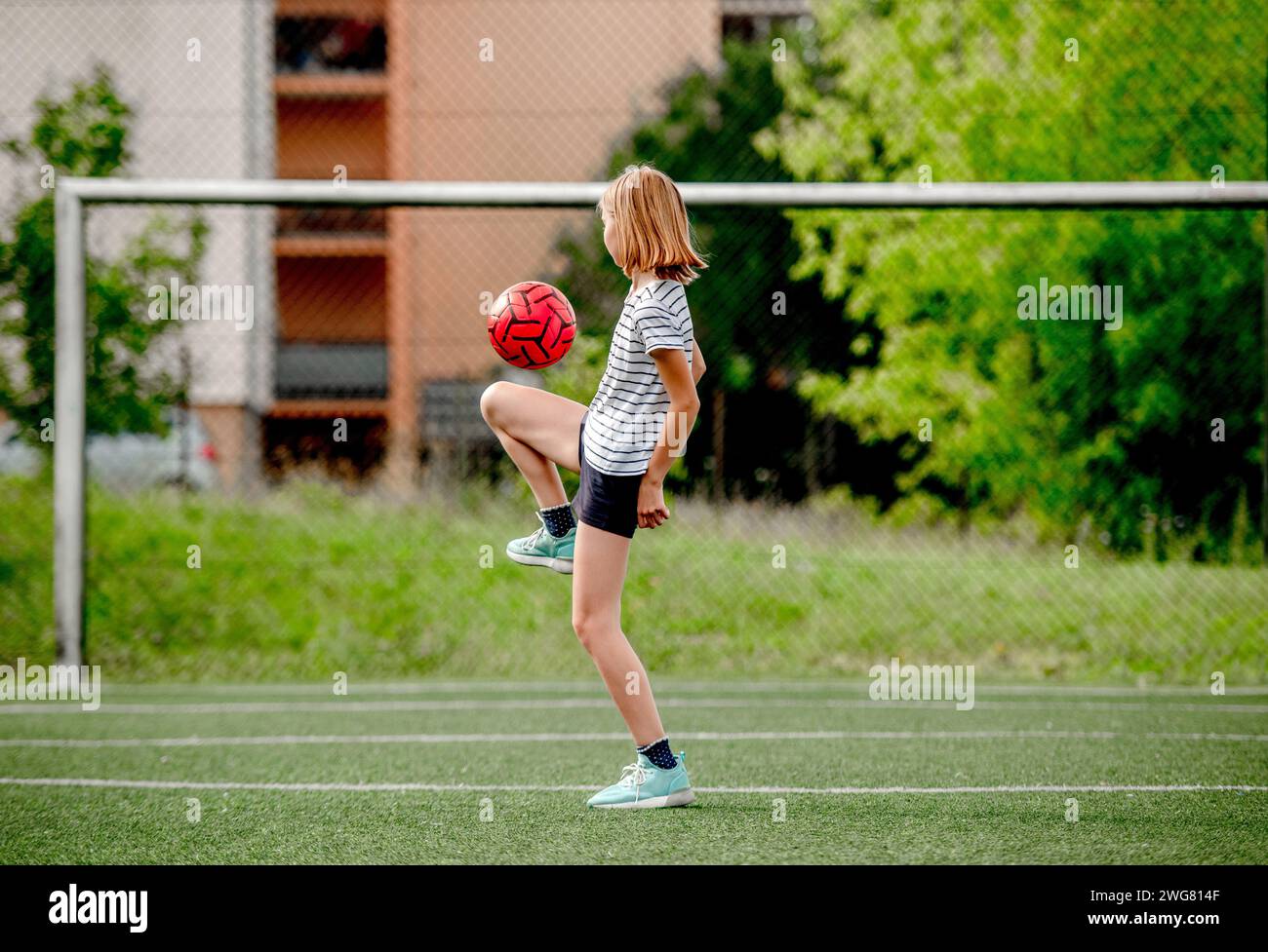 Pretty child girl kicking football ball at socket field. Cute female kid playing active game Stock Photo