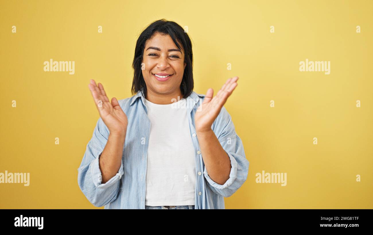 Hispanic woman clapping in front of a yellow background, expressing ...