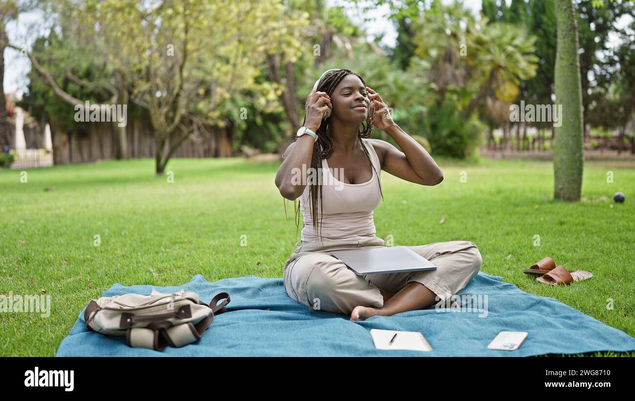 African american woman student using laptop and headphones at campus ...