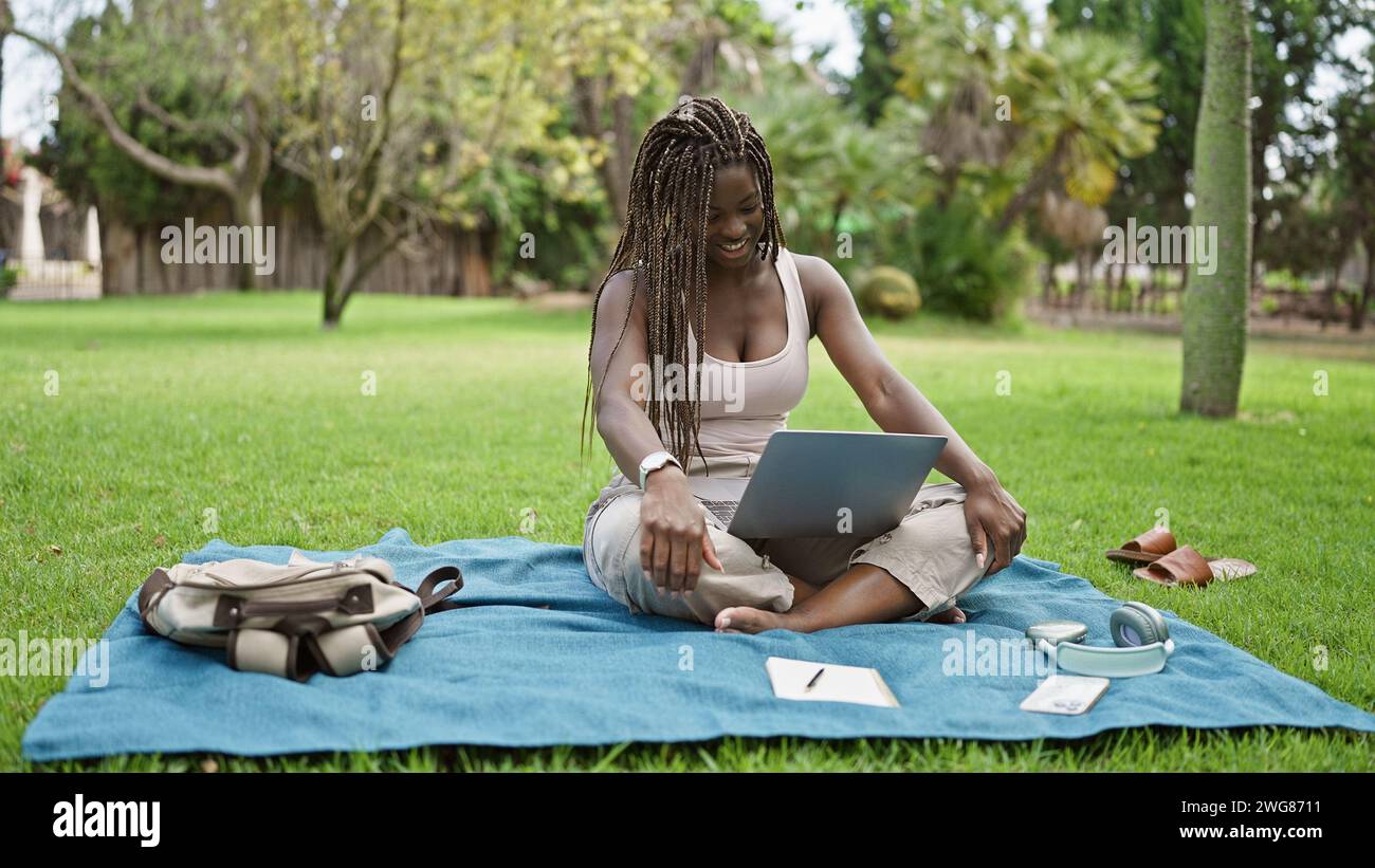 African american woman student using laptop smiling at campus ...