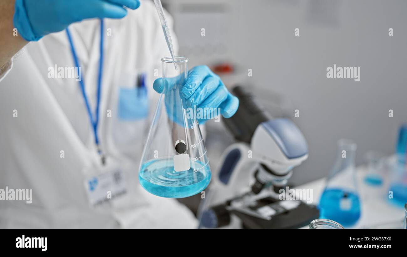 Caucasian male scientist pipetting blue liquid into a flask in a ...