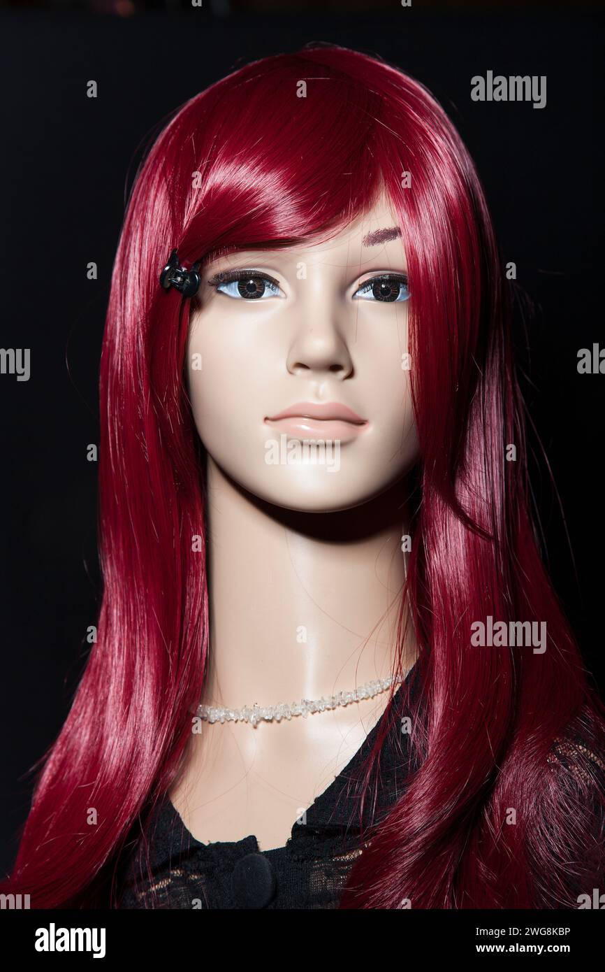 Plastic woman mannequin with bright long red hair posing on a black