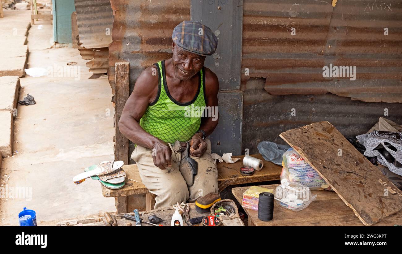 Shoe maker cobbler Nima Accra Ghana Africa poverty. Old Muslim shoe maker and cobbler. Poverty section of Accra Ghana. Primitive tools outdoors market. Stock Photo