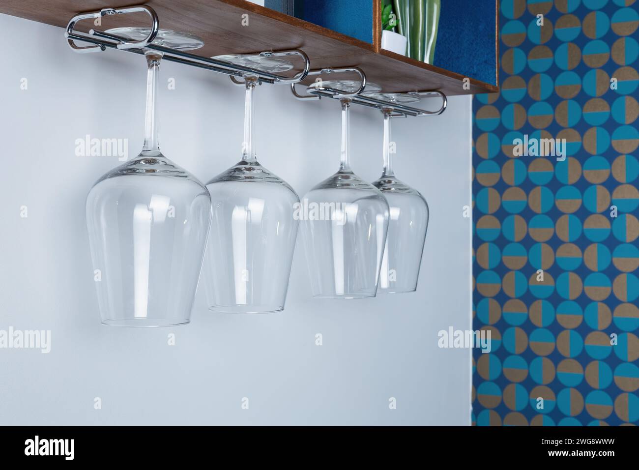 rystal wine glasses hang from a wooden rack. patterned retro wallpaper on the wall Stock Photo