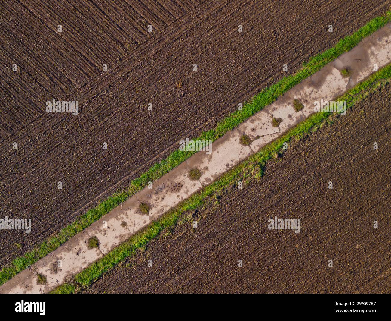 Plowed field with fertile soil forming a diagonal pattern with a dirt road, aerial view Stock Photo