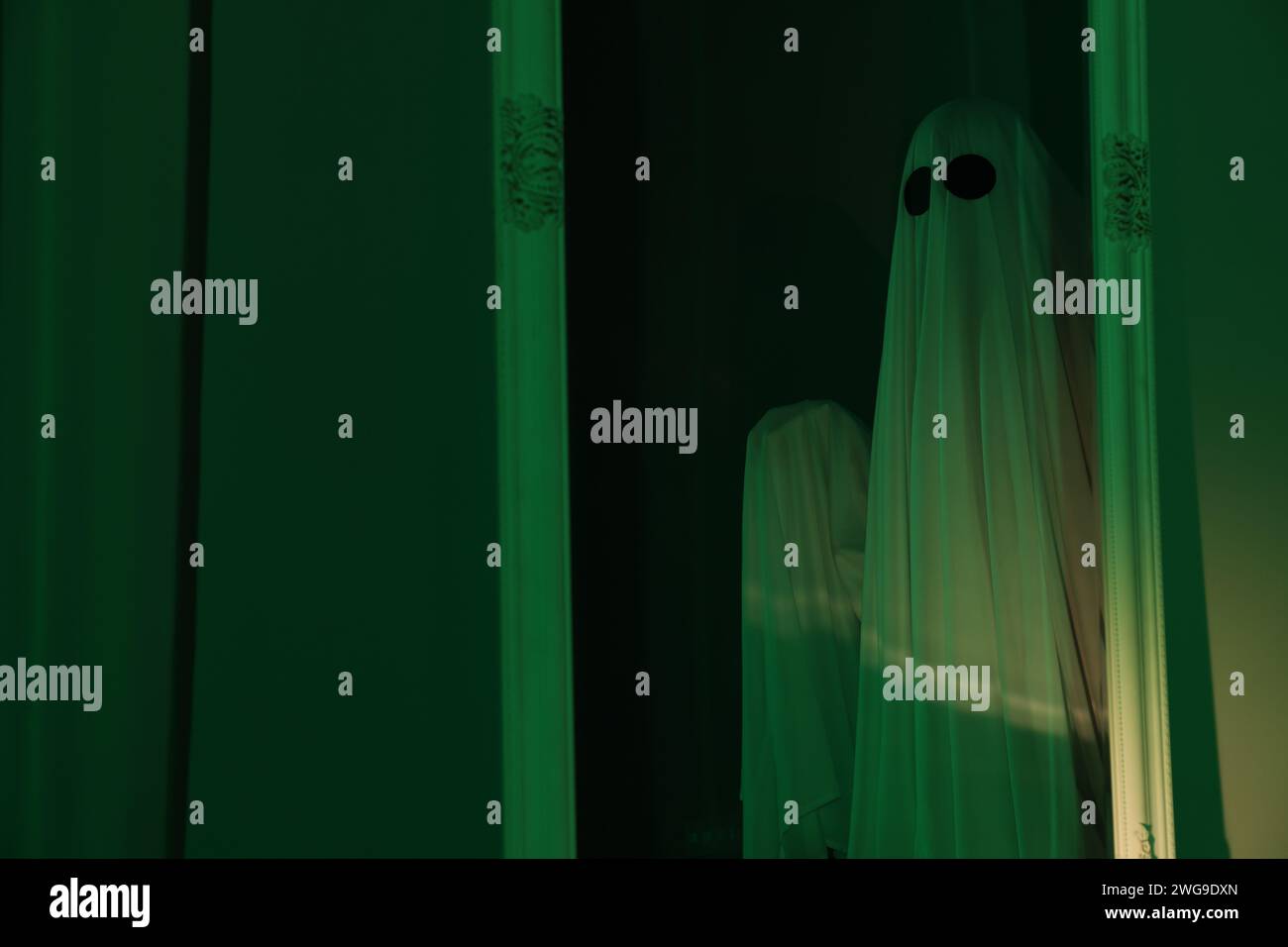 Creepy ghost. Woman covered with sheet in green light, reflection in ...