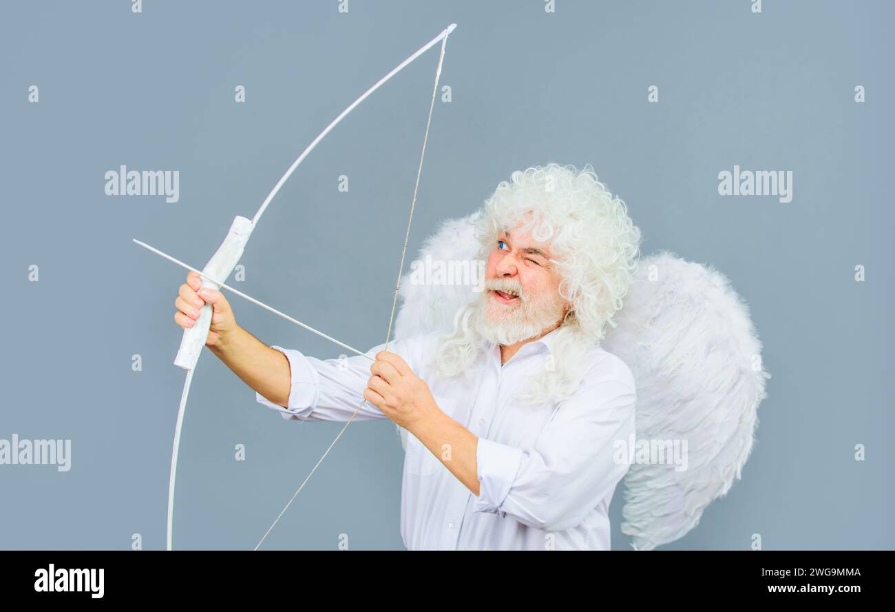 Valentine angel in white wig aiming with bow. Symbol of love. Valentines day cupid in angel wings shooting arrow of love. Handsome bearded man in Stock Photo