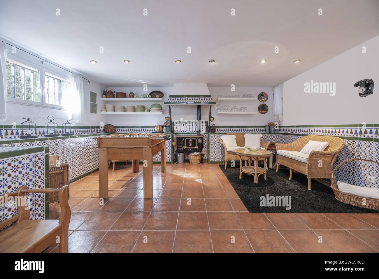 A cellar or games room with a table football, a cast iron kitchen with a fireplace and a wicker sofa in one corner Stock Photo