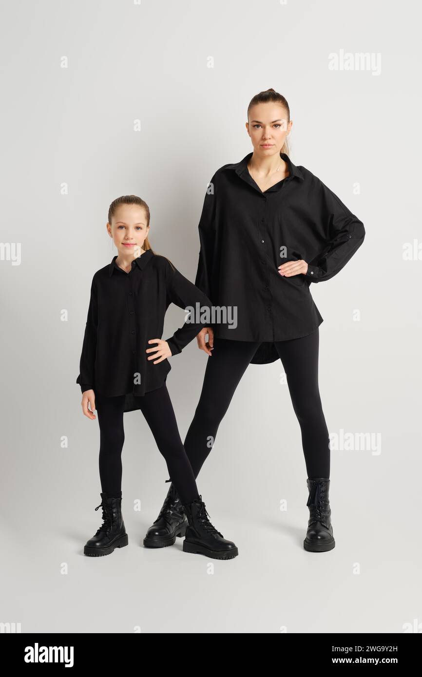 A modern family dressed in stylish black outfits poses confidently against a plain white background. The mother and her daughter are wearing matching Stock Photo