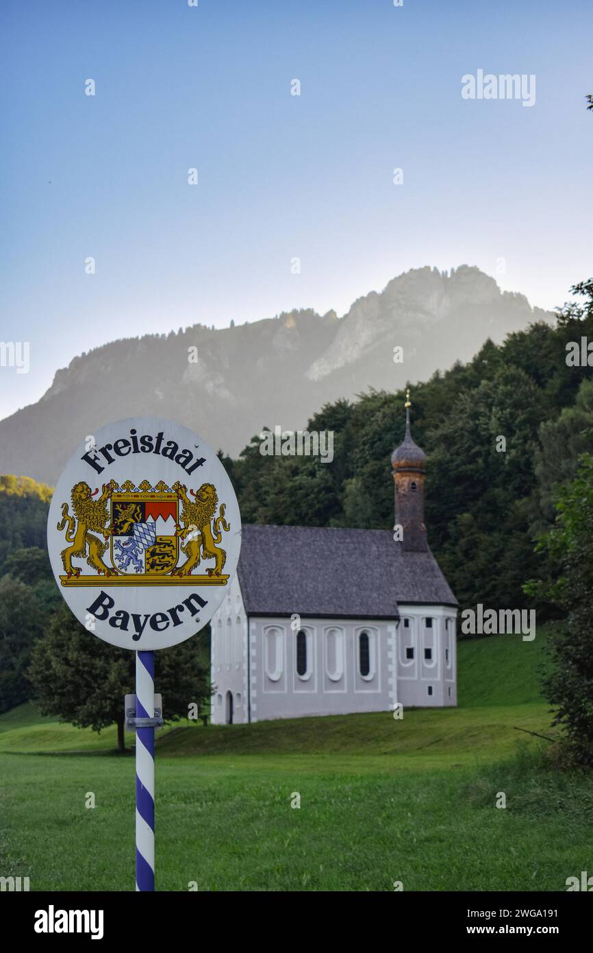A sign with the inscription 'Freistaat Bayern' in front of a church and a wooded mountain, Bavaria, Germany Stock Photo