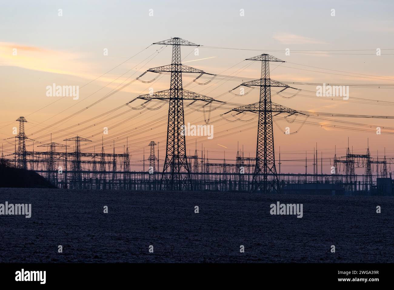 Electricity pylons towering into an orange-blue twilight sky, Wolmirstedt, Saxony-Anhalt, Germany Stock Photo