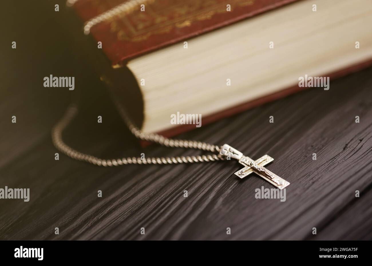 Silver necklace with crucifix cross on christian holy bible book on black wooden table. Asking blessings from God with the power of holiness, which brings luck and shows forgiveness. Stock Photo