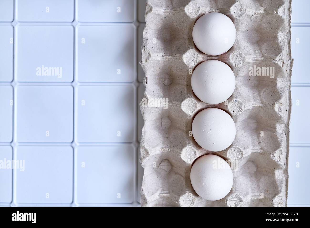 Four white eggs in a packing carton on a plastic surface Stock Photo